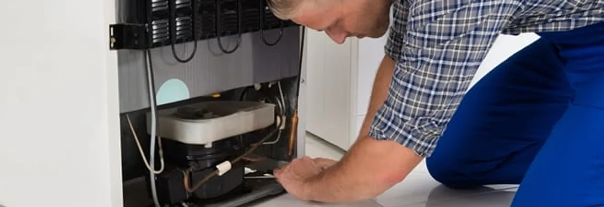 Refrigerator repair technician servicing the compressor and condenser area in Tuscaloosa, AL