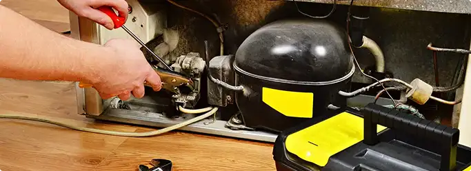 Refrigerator repair technician fixing the compressor and wiring in Tuscaloosa, AL